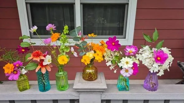 Six small arrangements in colored glass vases lined up on a porch rail