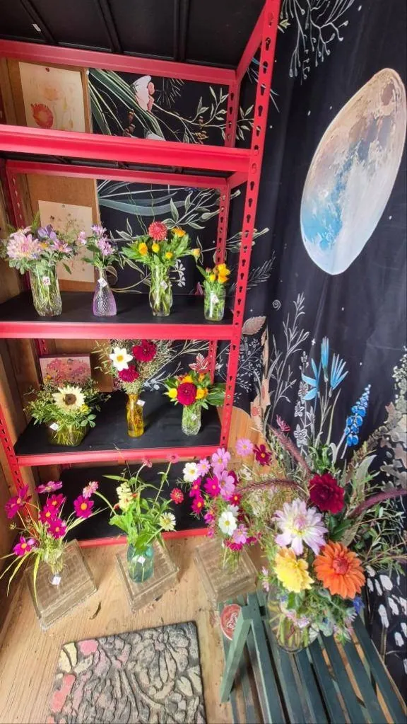 Inside the shed: red shelves of arrangements in front of a painted floral mural with a moon