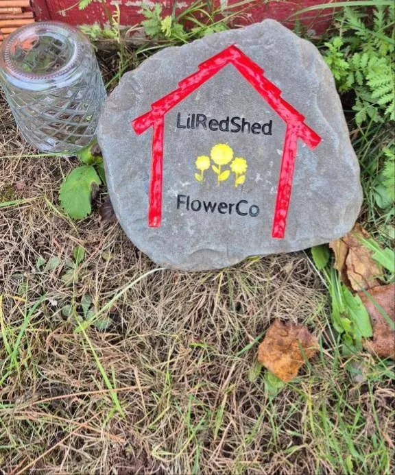 Painted stone with a red house outline and the words LilRedShedFlowerCo