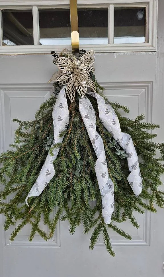 Evergreen swag with a silver poinsettia and printed ribbon hanging on a door