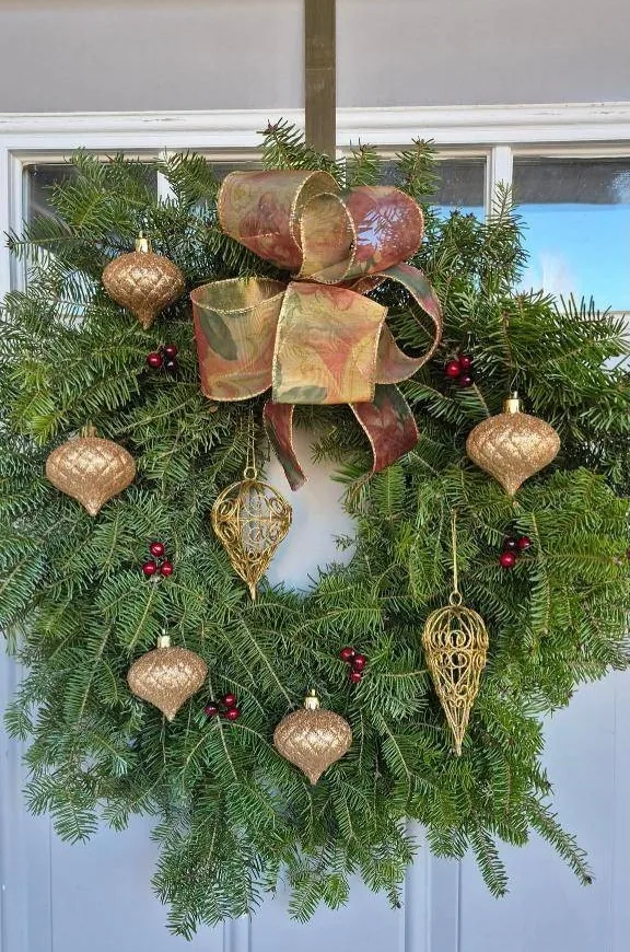 Balsam wreath with a gold and burgundy ribbon and gold ornaments on a white door